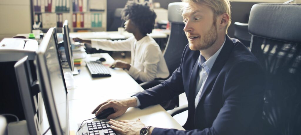 A photograph of a man working at a computer on a shared desk.