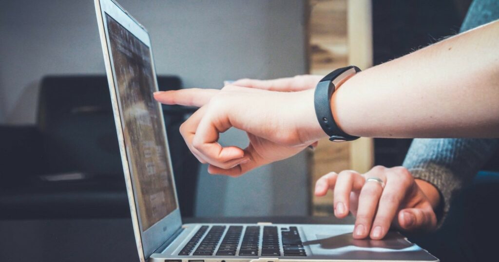 A photograph of one person working on a laptop while another points at the laptop screen.