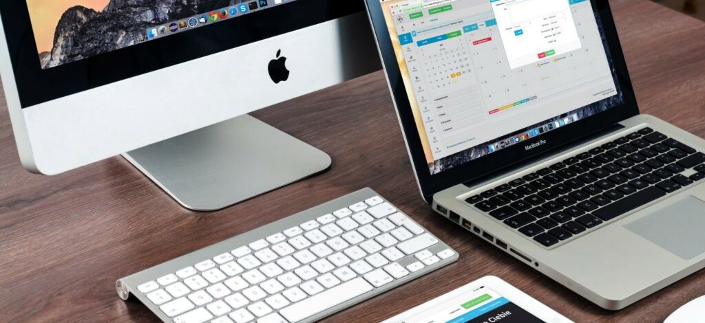 A photograph of a desk with a monitor, keyboard, and laptop on it.