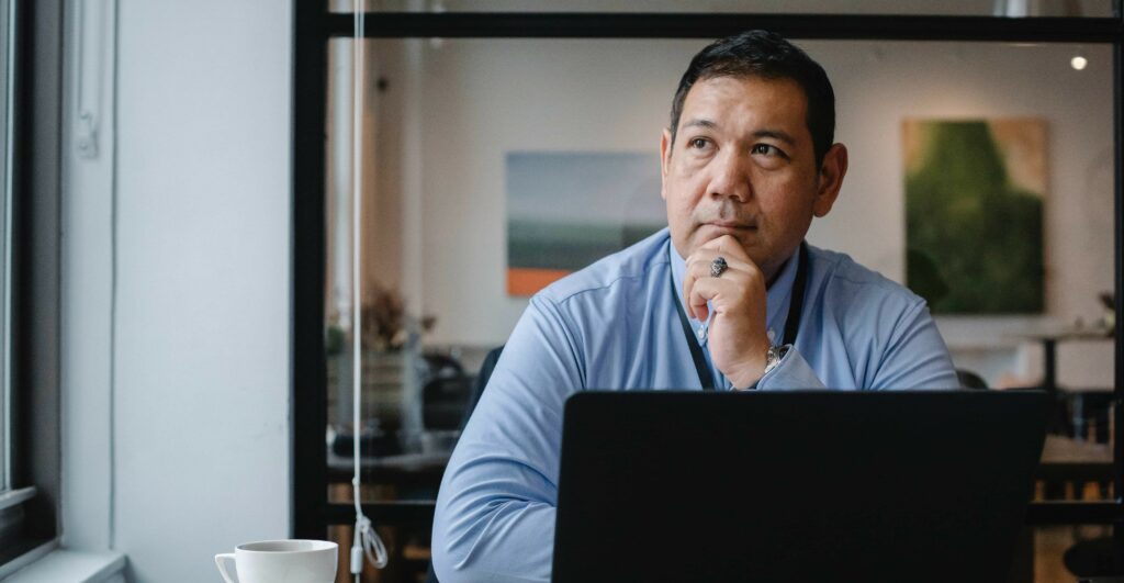 A man sits thoughtfully while he works on laptop