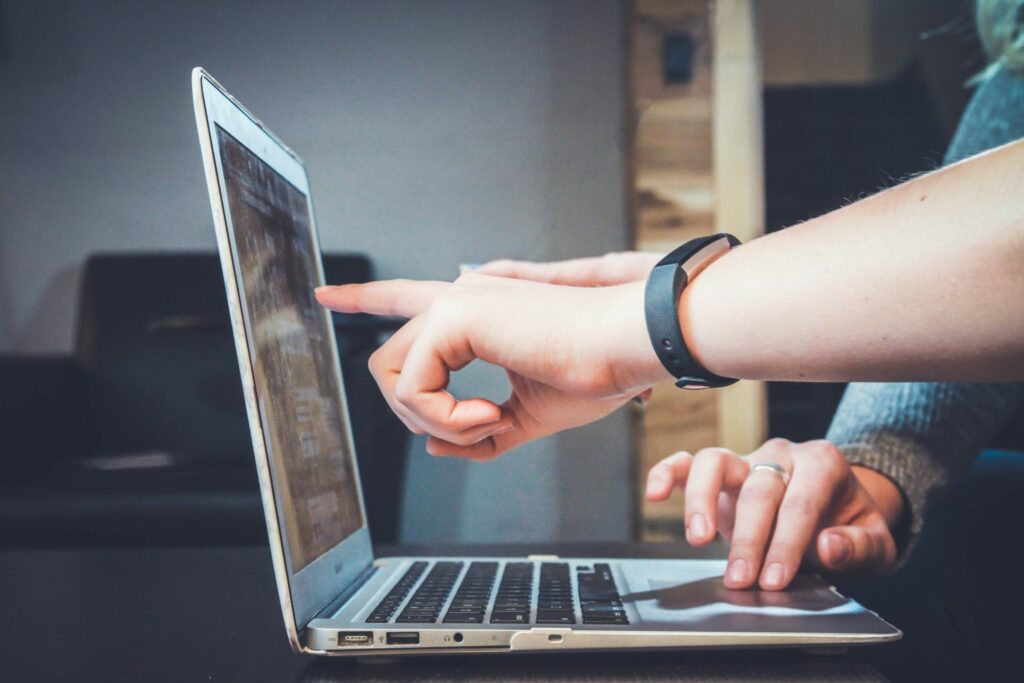 A photograph of one person working on a laptop and another pointing at the screen.