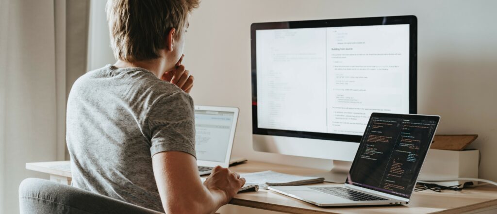 A man looks at a large computer monitor while working on two laptops.