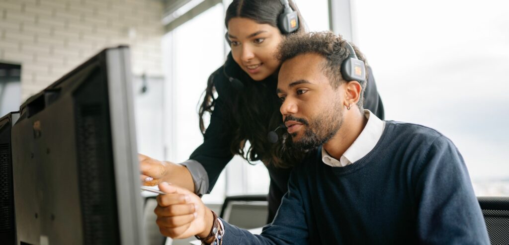A man and woman wearing headsets work on a computer together