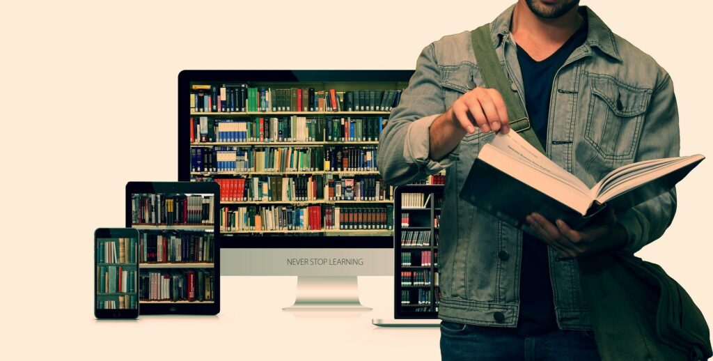 A photograph of a man reading a large book in front of a computer monitor, tablet, and smart phone all displaying images of books.