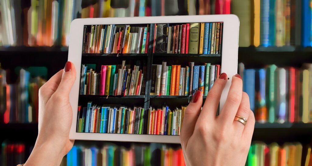A photograph of a woman holding up a tablet to take photos of books on a shelving unit.